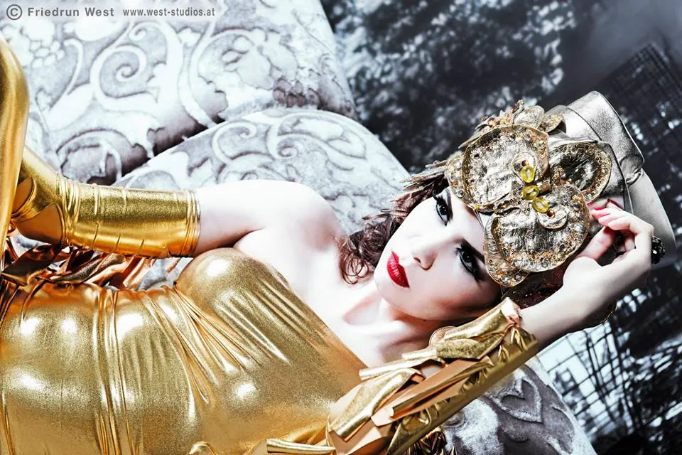 Model mit goldenem Kopfschmuck und Handschuhen liegend auf einem Sofa