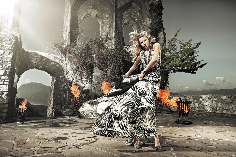 Model im gemusterten Kleid vor einer Ruine mit Feuerschalen