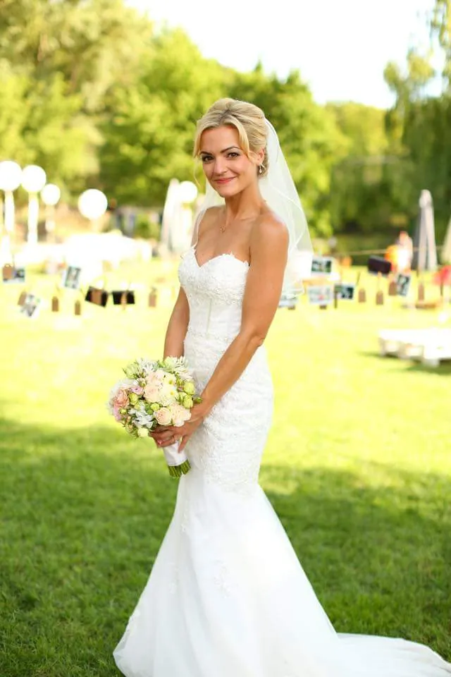 Braut im trägerlosen Kleid mit Brautstrauß auf einer Wiese