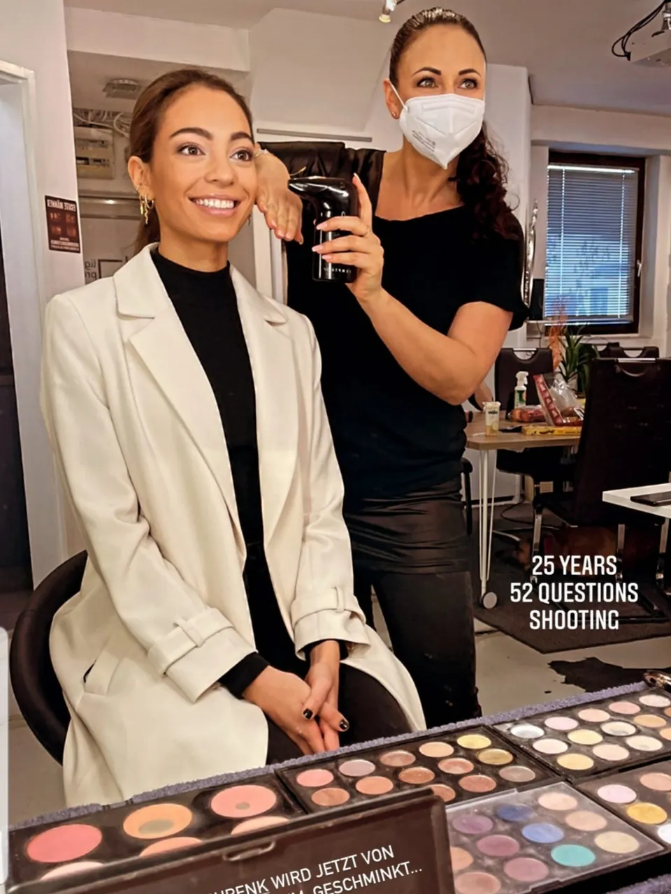 Martina Hirsch mit Maske schminkt eine Frau, Text-Einblendung „25 Years – 52 Questions – Shooting“